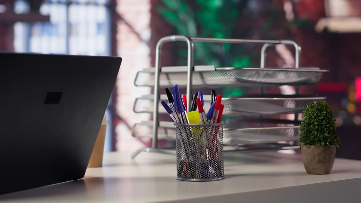 Escrivaninha de home office organizada com porta-canetas, bandeja de documentos, bloco de notas e monitor