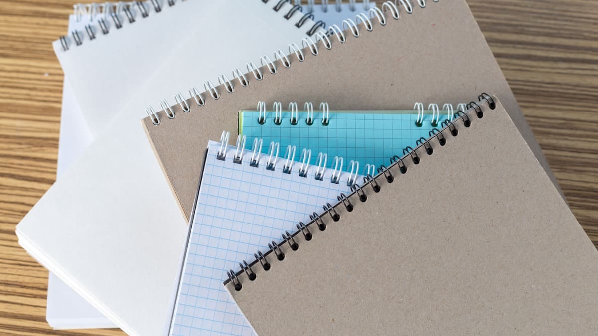 Pilha de cadernos universitários espiralados de capas diferentes sobre uma carteira escolar